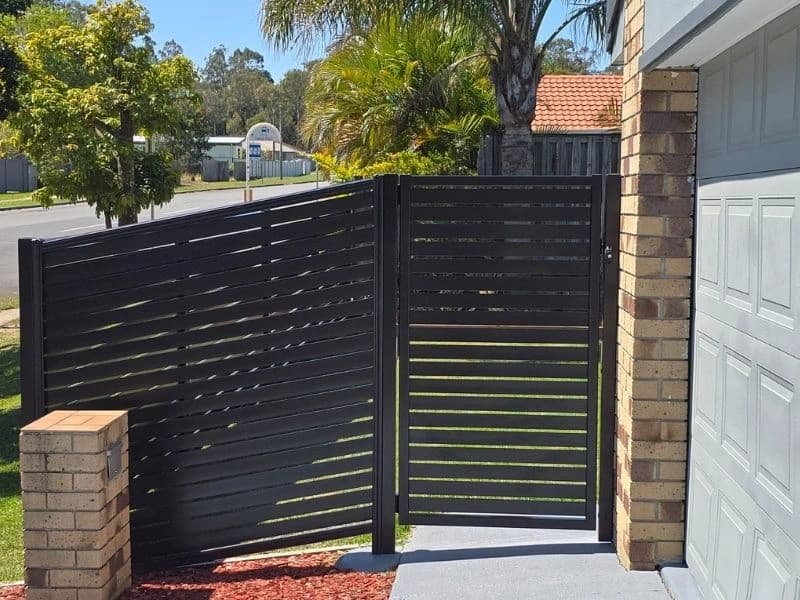 Black horizontal slat screen and matching gate beside a brick pier
